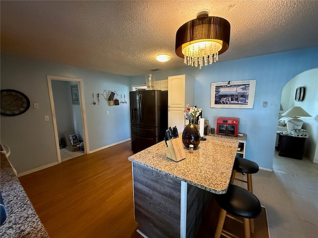 2424 Bates Ave SW, Winter Haven, FL 33880 - kitchen with black refrigerator with ice dispenser, a kitchen breakfast bar, a textured ceiling, baseboards, and wood finished floors
