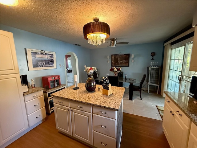 2424 Bates Ave SW, Winter Haven, FL 33880 - kitchen featuring arched walkways, dark wood-style floors, a kitchen island, a textured ceiling, and light stone countertops