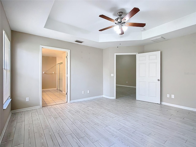 3806 Osprey Pointe Cir, Winter Haven, FL 33884 - unfurnished bedroom featuring a raised ceiling, light wood-style floors, connected bathroom, and ceiling fan