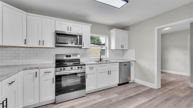 980 S Mill Ave, Bartow, FL 33830 - kitchen featuring appliances with stainless steel finishes, white cabinets, light stone countertops, backsplash, and light wood finished floors
