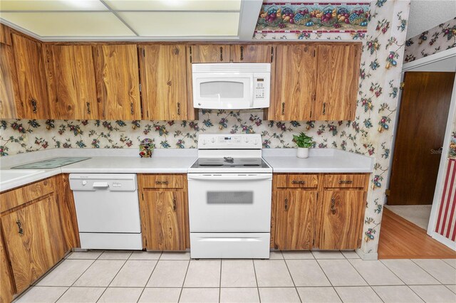 3315 Cross Fox Dr, Mulberry, FL 33860 - kitchen with white appliances, wallpapered walls, light countertops, brown cabinets, and light tile patterned floors