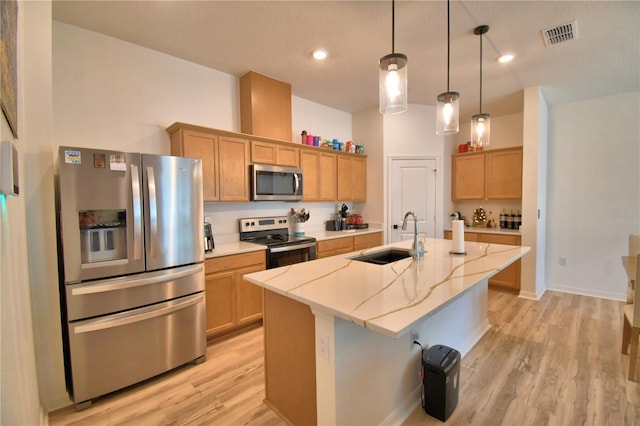 312 Walnut Ln, Auburndale, FL 33823 - kitchen featuring appliances with stainless steel finishes, light wood-style flooring, a center island with sink, light stone counters, and decorative light fixtures