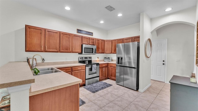 6365 Torrington Cir, Lakeland, FL 33811 - kitchen with stainless steel appliances, a peninsula, arched walkways, light tile patterned floors, and brown cabinetry