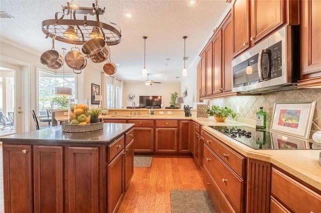 2026 Indian Sky Cir, Lakeland, FL 33813 - kitchen featuring stainless steel microwave, black electric cooktop, light wood-style flooring, brown cabinetry, and crown molding