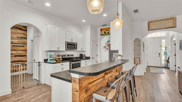 1028 15th St NE, Winter Haven, FL 33881 - kitchen featuring stainless steel appliances, dark countertops, arched walkways, light wood-style floors, and a kitchen breakfast bar