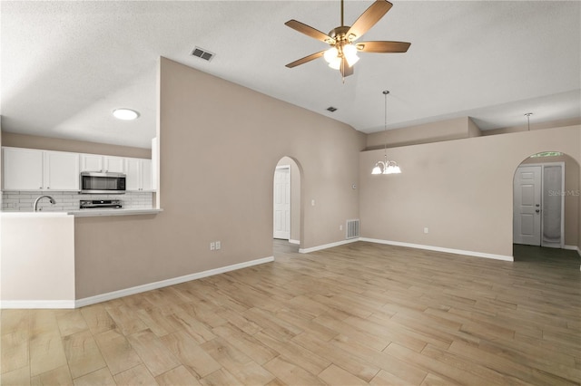 1125 Blackjack Ridge St, Minneola, FL 34715 - unfurnished living room featuring arched walkways, a ceiling fan, light wood finished floors, a chandelier, and high vaulted ceiling