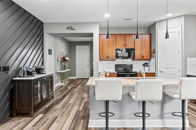 180 Azure Mist Way, Daytona Beach, FL 32124 - kitchen featuring black appliances, wood finished floors, light stone countertops, an island with sink, and a breakfast bar