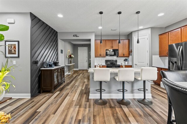 180 Azure Mist Way, Daytona Beach, FL 32124 - kitchen with black appliances, brown cabinets, light wood-type flooring, a kitchen island with sink, and decorative light fixtures