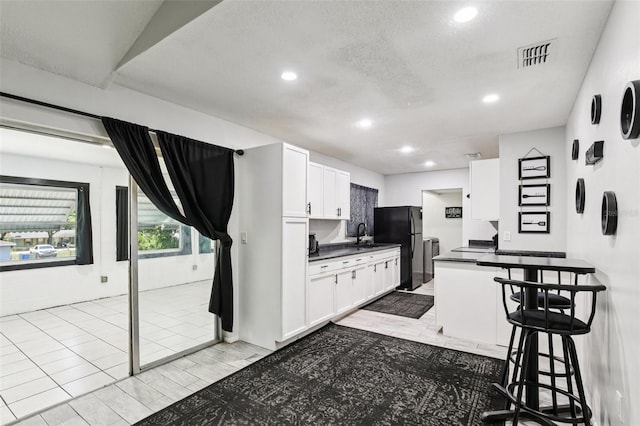 3854 Feather Dr, Lakeland, FL 33812 - kitchen featuring dark countertops, freestanding refrigerator, white cabinets, a breakfast bar, and recessed lighting