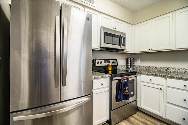 3542 Raintree Ct, Lakeland, FL 33803 - kitchen featuring appliances with stainless steel finishes, white cabinets, light wood finished floors, light stone countertops, and a textured ceiling