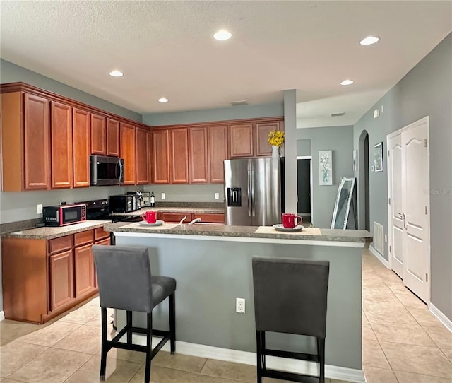 13303 Moss Park Ridge Dr, Orlando, FL 32832 - kitchen featuring appliances with stainless steel finishes, light tile patterned flooring, recessed lighting, a center island with sink, and a breakfast bar