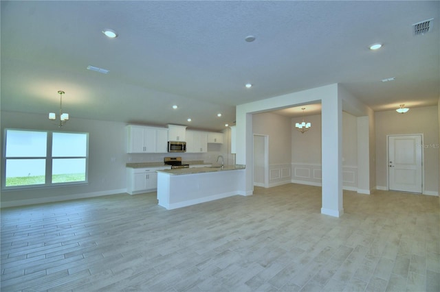 5427 Waterside Dr, Auburndale, FL 33823 - kitchen with a chandelier, stainless steel appliances, open floor plan, light wood-style floors, and white cabinetry