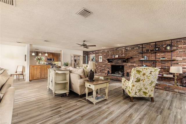 521 Lone Palm Dr, Lakeland, FL 33815 - living room featuring light wood-style flooring, a textured ceiling, a ceiling fan, a brick fireplace, and brick wall
