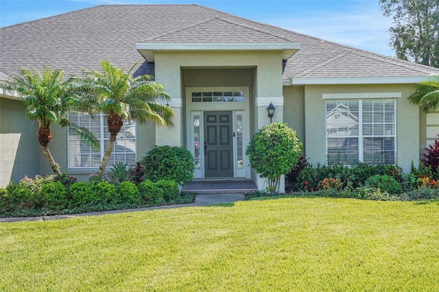 122 Amber Blvd, Auburndale, FL 33823 - doorway to property featuring a lawn, stucco siding, and roof with shingles