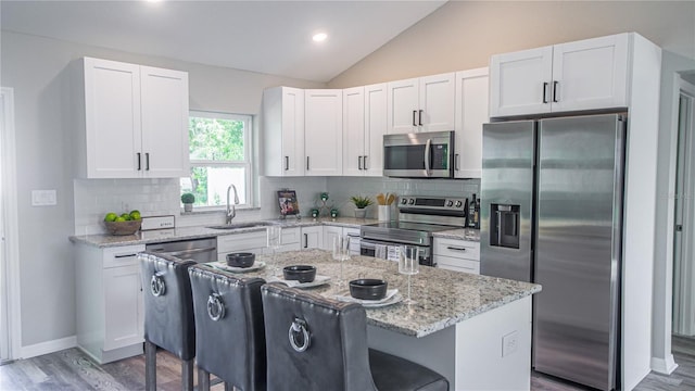 6262 NW 61st St, Ocala, FL 34482 - kitchen featuring appliances with stainless steel finishes, vaulted ceiling, a breakfast bar area, white cabinets, and light stone counters