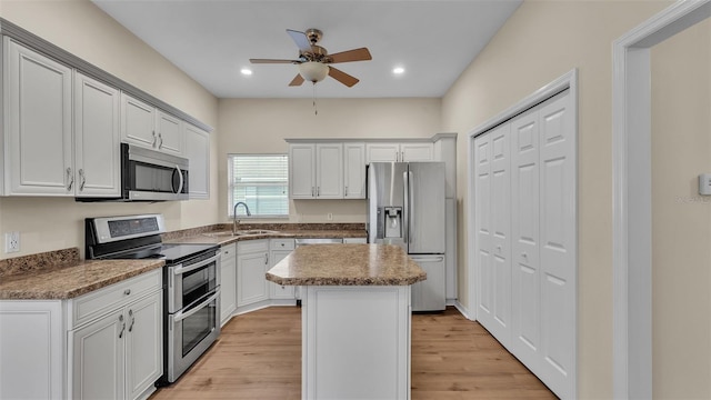 4445 Pebble Pointe Dr, Lakeland, FL 33813 - kitchen with stainless steel appliances, a ceiling fan, a center island, light wood-style flooring, and white cabinets