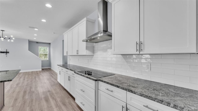 1095 Woodland Oaks Dr, Lakeland, FL 33813 - kitchen with wall chimney exhaust hood, black electric stovetop, dark stone countertops, white cabinetry, and light wood-type flooring