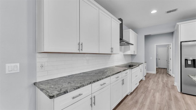 1095 Woodland Oaks Dr, Lakeland, FL 33813 - kitchen with wall chimney exhaust hood, stainless steel fridge, black electric cooktop, white cabinetry, and dark stone counters