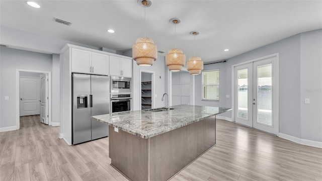 1095 Woodland Oaks Dr, Lakeland, FL 33813 - kitchen with built in appliances, light stone counters, light wood-type flooring, white cabinetry, and an island with sink