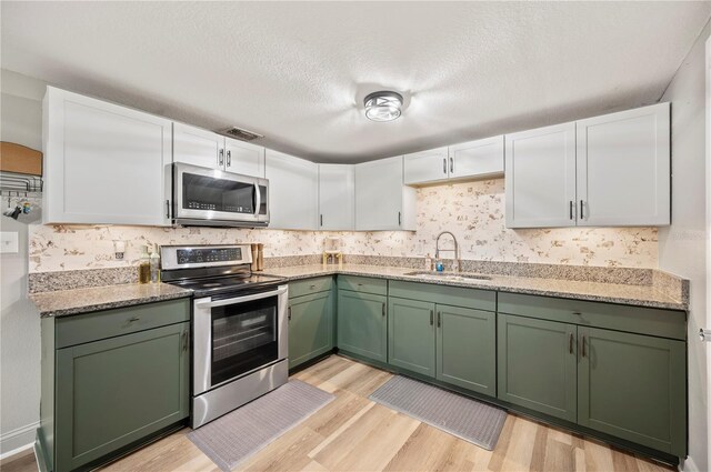 1231 Melville Ave, Lakeland, FL 33805 - kitchen featuring appliances with stainless steel finishes, green cabinetry, light wood-type flooring, white cabinets, and backsplash