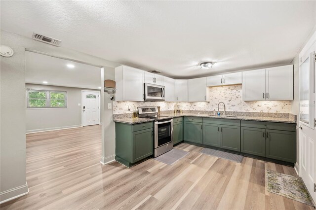 1231 Melville Ave, Lakeland, FL 33805 - kitchen featuring appliances with stainless steel finishes, green cabinets, light wood finished floors, and decorative backsplash