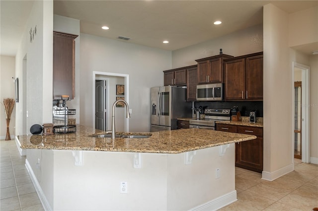702 Country Walk Cv, Eagle Lake, FL 33839 - kitchen featuring stainless steel appliances, dark brown cabinetry, a breakfast bar area, light tile patterned flooring, and light stone countertops