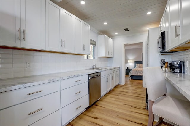 kitchen with appliances with stainless steel finishes, light hardwood / wood-style floors, white cabinets, light stone counters, and tasteful backsplash