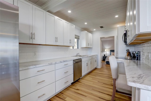 kitchen with appliances with stainless steel finishes, light stone countertops, tasteful backsplash, white cabinetry, and light wood-type flooring