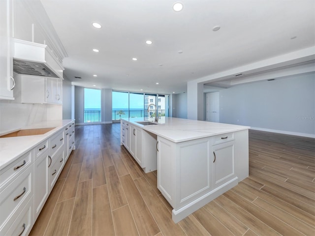 kitchen featuring white cabinetry, sink, an island with sink, and light hardwood / wood-style flooring