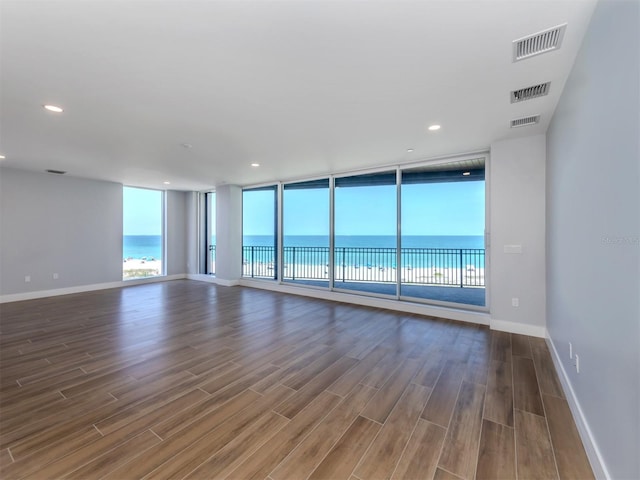 spare room featuring expansive windows, a water view, and dark wood-type flooring