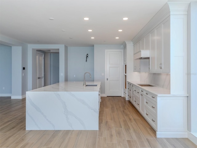 kitchen featuring light stone countertops, light hardwood / wood-style floors, white cabinetry, and sink