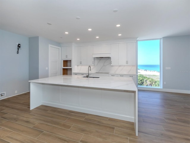 kitchen with white cabinetry, a large island, light stone countertops, and light wood-type flooring