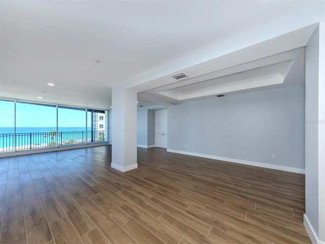 unfurnished room with a raised ceiling, dark hardwood / wood-style flooring, and a water view