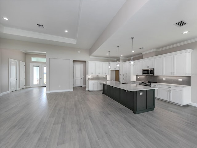 kitchen featuring appliances with stainless steel finishes, white cabinets, a kitchen island with sink, and light wood-type flooring