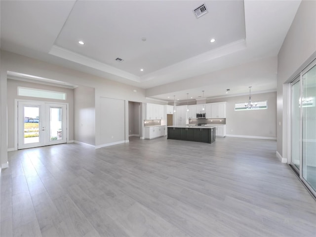 unfurnished living room featuring french doors, a notable chandelier, light wood-type flooring, and a raised ceiling