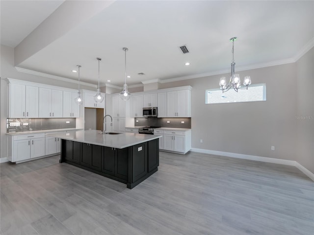 kitchen with an island with sink, stainless steel appliances, sink, decorative light fixtures, and white cabinets