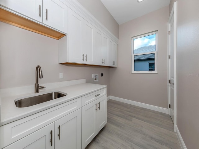 laundry area featuring electric dryer hookup, hookup for a washing machine, sink, light wood-type flooring, and cabinets