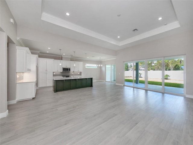 unfurnished living room featuring sink, light hardwood / wood-style flooring, a notable chandelier, and a raised ceiling