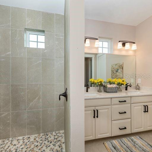 bathroom with dual vanity, tiled shower, and plenty of natural light