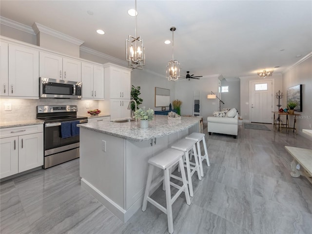 kitchen with white cabinetry, ceiling fan, an island with sink, light stone counters, and appliances with stainless steel finishes