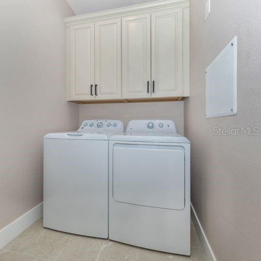 laundry room featuring washing machine and dryer, cabinets, and light tile patterned floors