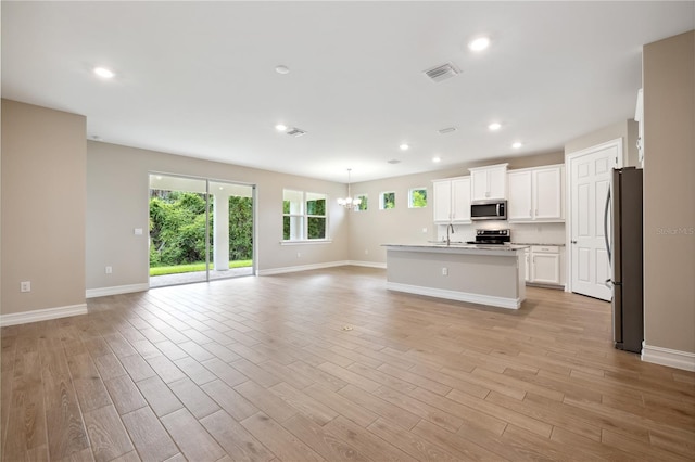 kitchen featuring open floor plan, stainless steel appliances, a sink, and light wood-style flooring