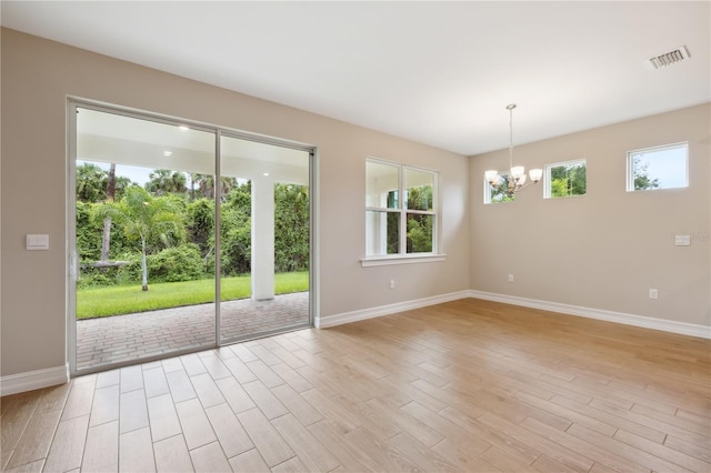 spare room with light wood finished floors, baseboards, visible vents, and a chandelier