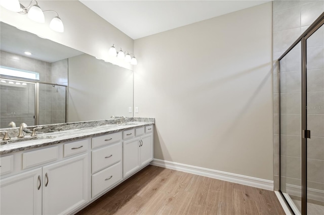 full bathroom with double vanity, a stall shower, a sink, wood finished floors, and baseboards