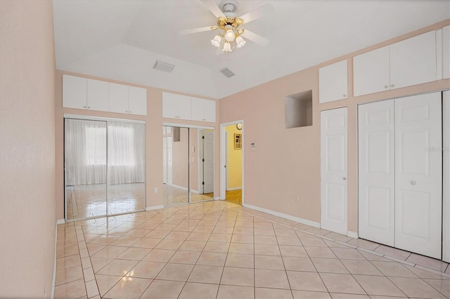 unfurnished bedroom featuring ceiling fan, light tile patterned flooring, multiple closets, and a tray ceiling