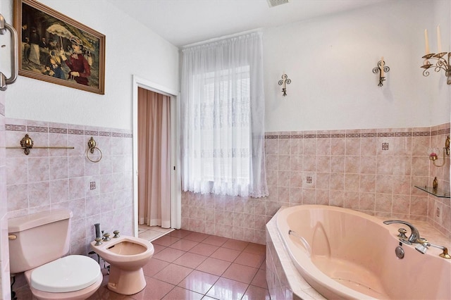 bathroom with toilet, tile walls, tile patterned flooring, tiled tub, and a bidet