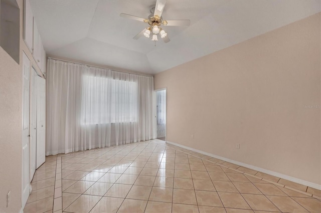 tiled empty room featuring ceiling fan, a tray ceiling, and lofted ceiling