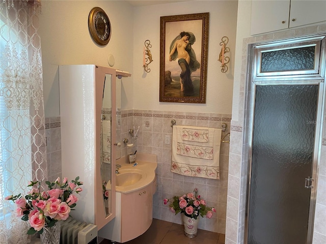 bathroom with a shower with door, radiator, tile walls, and vanity