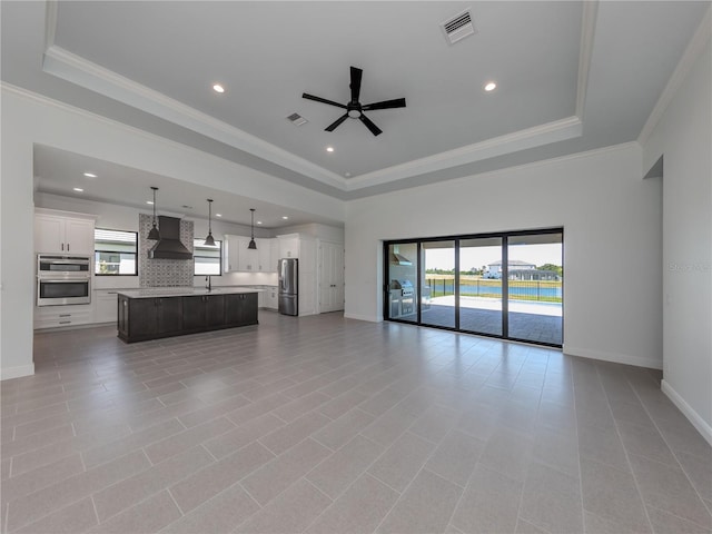 unfurnished living room with ceiling fan, a tray ceiling, light tile flooring, and ornamental molding