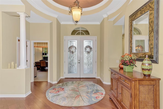 entrance foyer featuring french doors, ornate columns, ornamental molding, a tray ceiling, and light hardwood / wood-style floors